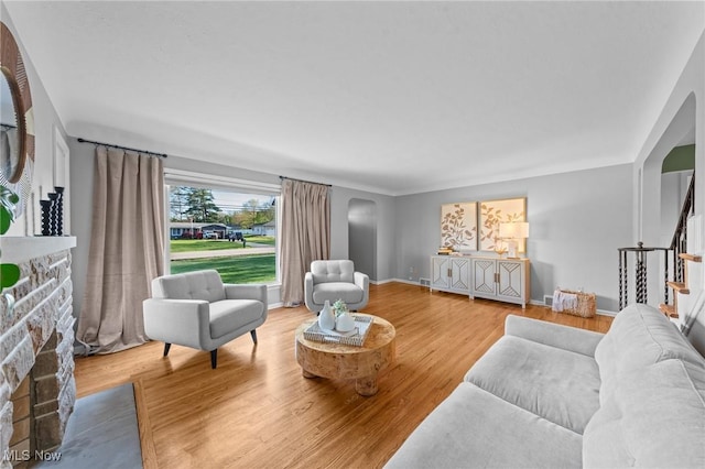 living area featuring a fireplace, arched walkways, stairs, baseboards, and wood finished floors