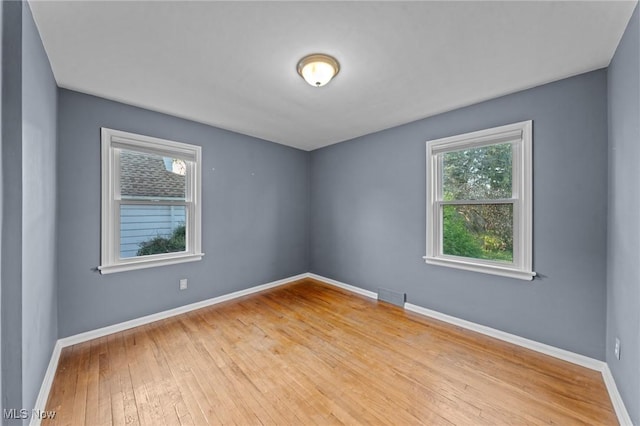 unfurnished room with a healthy amount of sunlight, baseboards, wood-type flooring, and visible vents