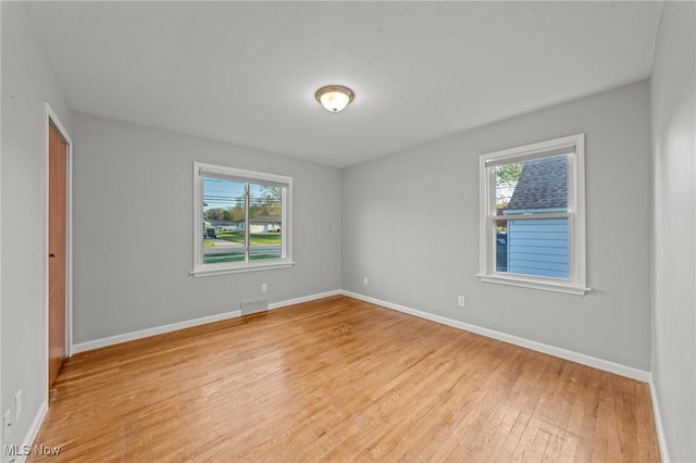 spare room featuring visible vents, light wood finished floors, baseboards, and a healthy amount of sunlight