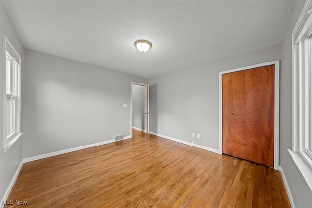 unfurnished bedroom featuring baseboards, visible vents, multiple windows, and wood finished floors
