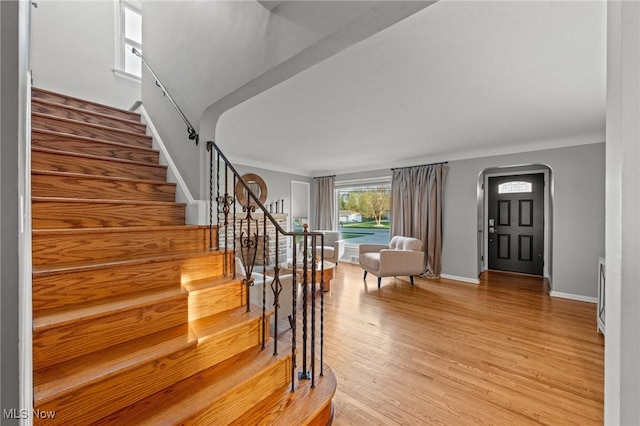 entrance foyer with light wood-type flooring, arched walkways, stairs, and baseboards