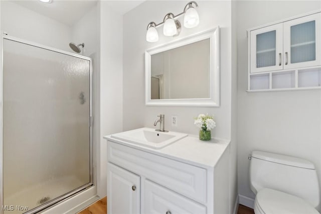 bathroom featuring vanity, a shower stall, toilet, and wood finished floors