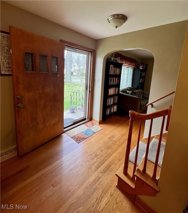 foyer featuring stairs, arched walkways, baseboards, and light wood-type flooring