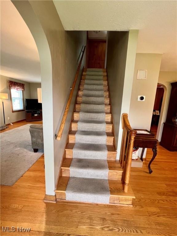 staircase with arched walkways and wood finished floors