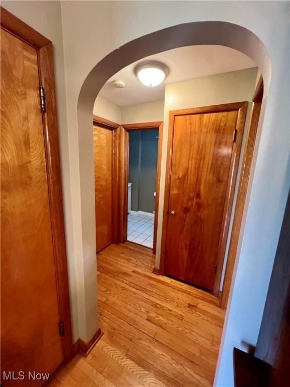 corridor featuring light wood-type flooring and arched walkways