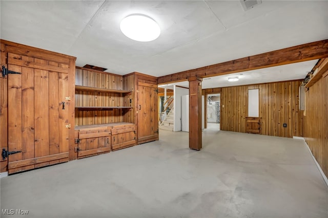 unfurnished living room with visible vents, finished concrete flooring, wooden walls, and stairway