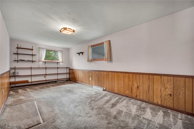 carpeted spare room featuring wooden walls and a wainscoted wall
