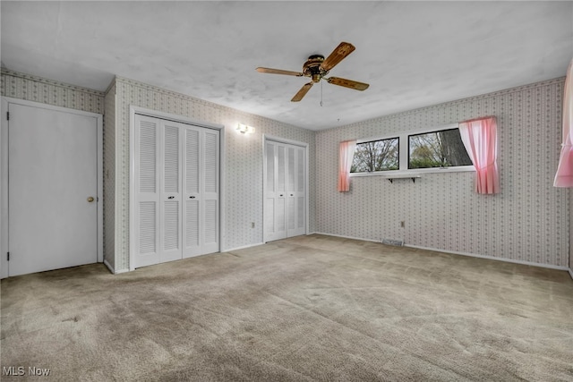 unfurnished bedroom featuring carpet floors, multiple closets, and wallpapered walls