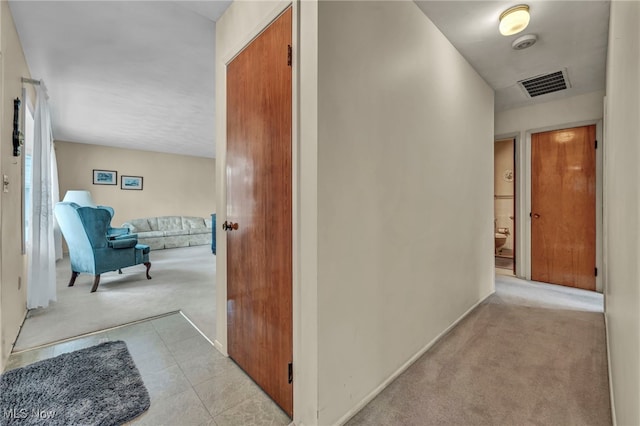 hall featuring baseboards, visible vents, and light carpet