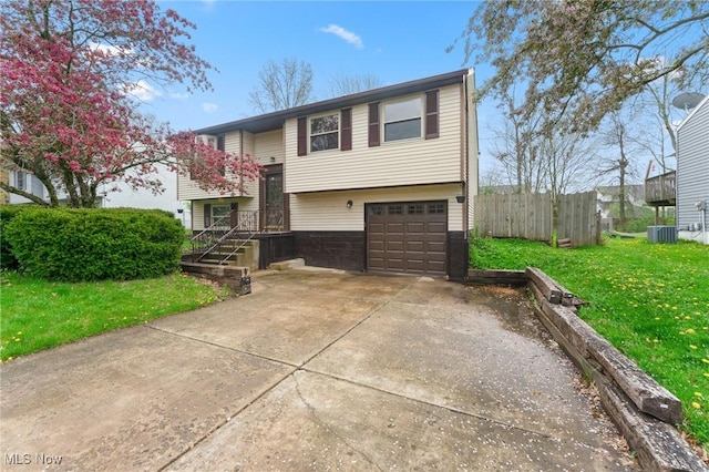 raised ranch featuring a garage, central AC, fence, a front lawn, and concrete driveway
