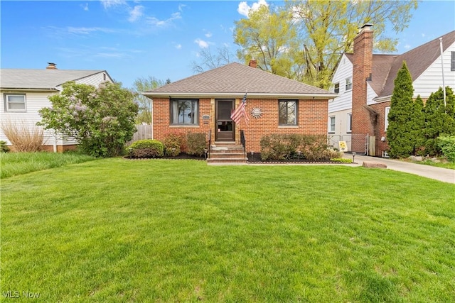 view of front facade featuring brick siding, fence, a shingled roof, and a front lawn