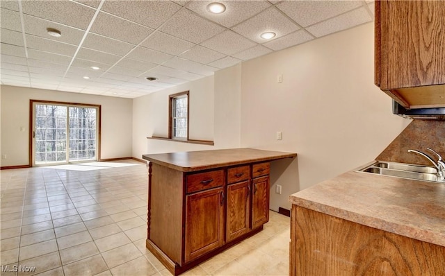 kitchen featuring light tile patterned floors, baseboards, a drop ceiling, and a sink