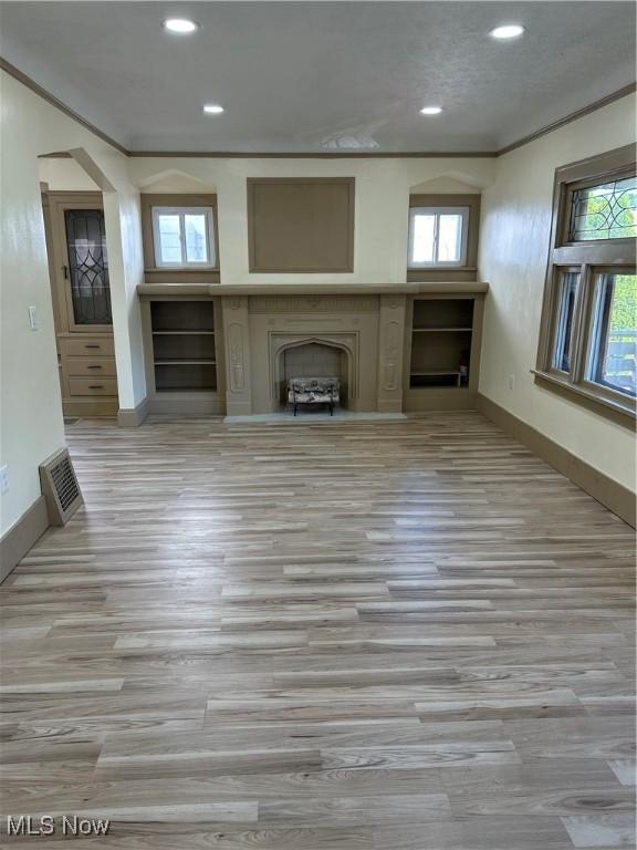 unfurnished living room with crown molding, a fireplace, recessed lighting, baseboards, and wood finished floors