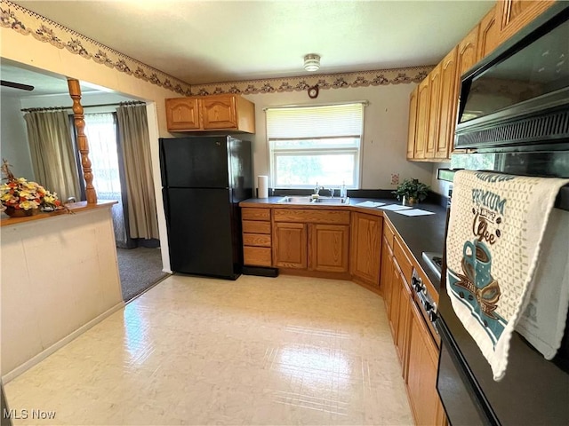 kitchen with a sink, light floors, black appliances, and dark countertops