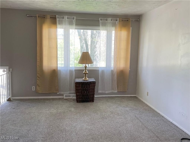 carpeted spare room with a textured ceiling, baseboards, and visible vents