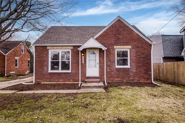 view of front of house with a front lawn, fence, roof with shingles, brick siding, and entry steps
