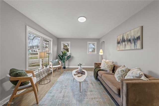 living room featuring arched walkways, baseboards, and wood finished floors