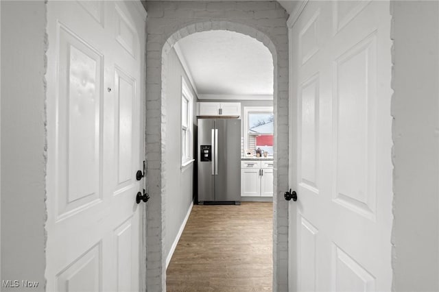 hallway with arched walkways and light wood-style floors