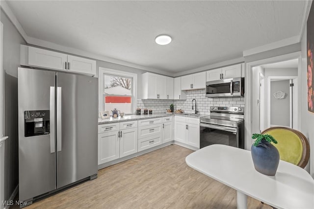 kitchen featuring white cabinetry, tasteful backsplash, a sink, light wood finished floors, and stainless steel appliances
