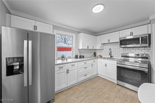 kitchen with a sink, appliances with stainless steel finishes, white cabinets, and light wood-type flooring