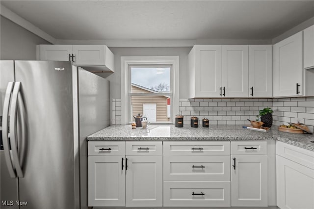 kitchen with light stone counters, decorative backsplash, white cabinetry, and stainless steel fridge with ice dispenser