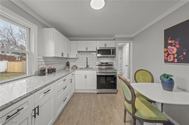 kitchen with a healthy amount of sunlight, white cabinets, backsplash, and stainless steel appliances