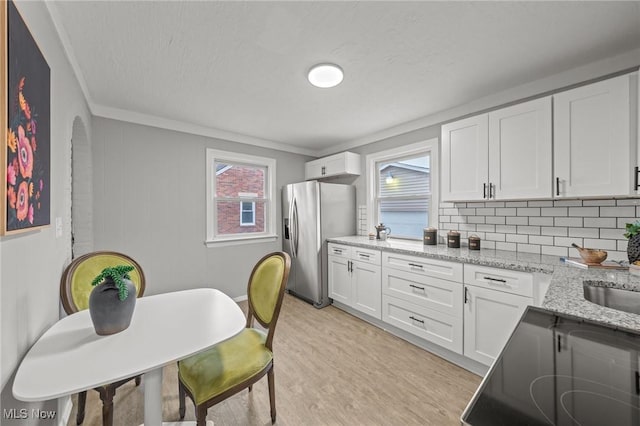 kitchen with stainless steel fridge, white cabinets, light wood finished floors, and black electric stovetop