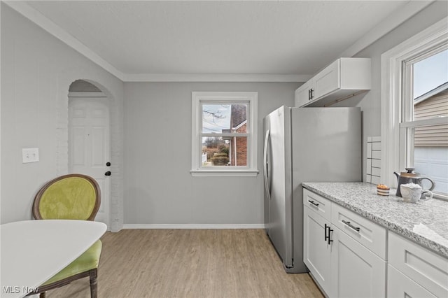 kitchen with freestanding refrigerator, baseboards, white cabinets, light stone counters, and light wood finished floors
