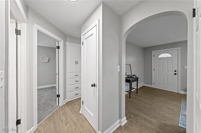 foyer with baseboards, arched walkways, and wood finished floors