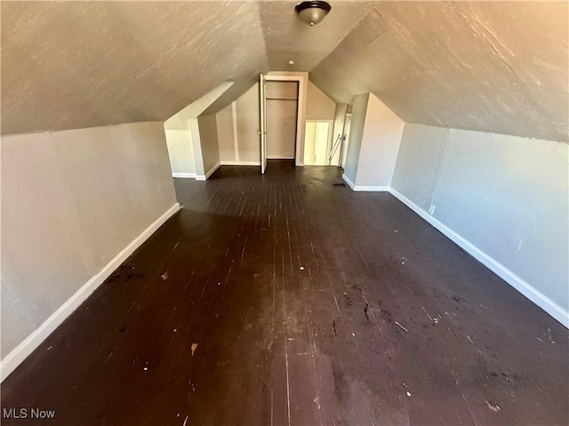 additional living space with baseboards, dark wood-style floors, and lofted ceiling