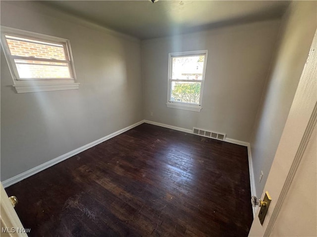 spare room with baseboards, visible vents, and dark wood finished floors