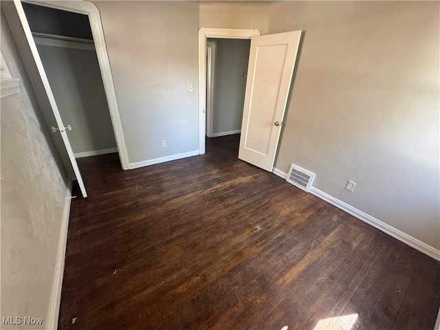 unfurnished bedroom with visible vents, baseboards, dark wood-style floors, and a closet