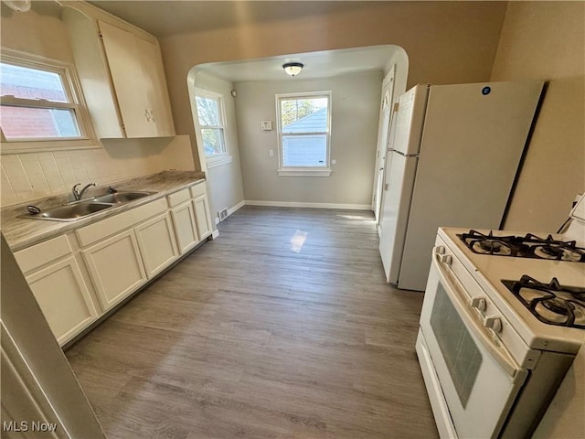 kitchen with a sink, light wood-style flooring, baseboards, white range with gas stovetop, and tasteful backsplash
