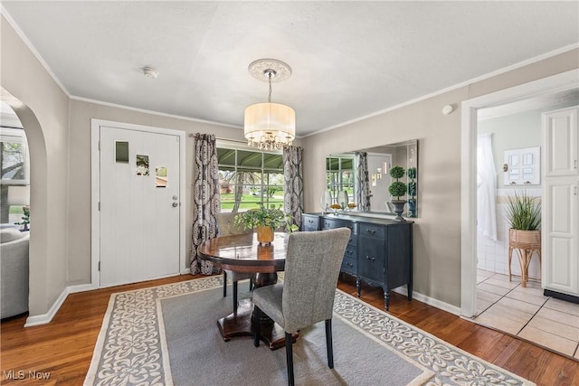 dining room featuring a healthy amount of sunlight, ornamental molding, wood finished floors, and a notable chandelier