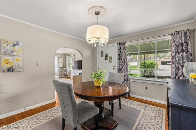 dining room featuring arched walkways, baseboards, ornamental molding, and wood finished floors