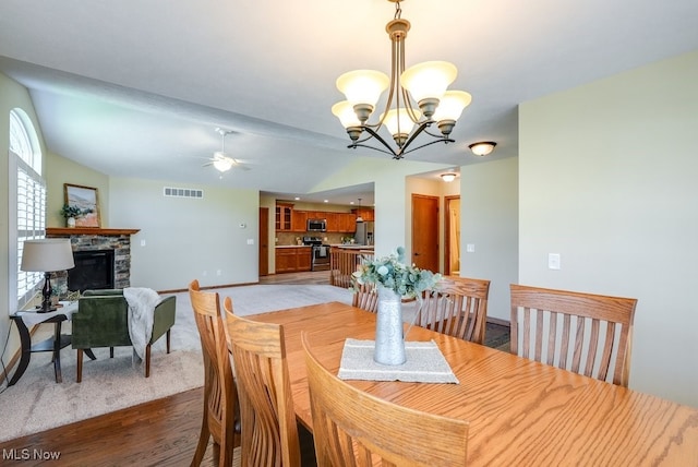 dining space featuring a stone fireplace, light wood-type flooring, baseboards, ceiling fan with notable chandelier, and lofted ceiling