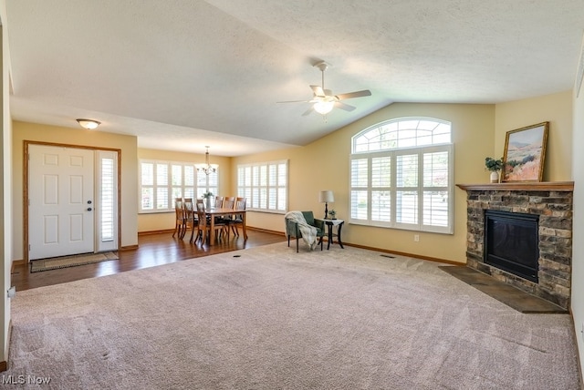 living area featuring a fireplace, baseboards, carpet flooring, ceiling fan with notable chandelier, and vaulted ceiling