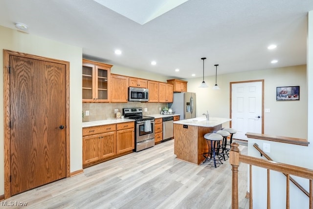 kitchen featuring appliances with stainless steel finishes, light countertops, light wood finished floors, a breakfast bar, and an island with sink