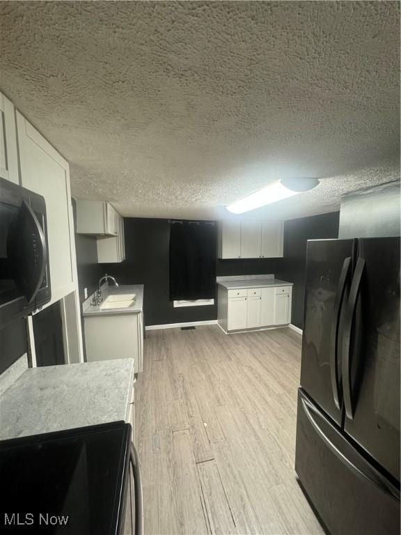 kitchen with a sink, light wood-style floors, range, freestanding refrigerator, and white cabinetry