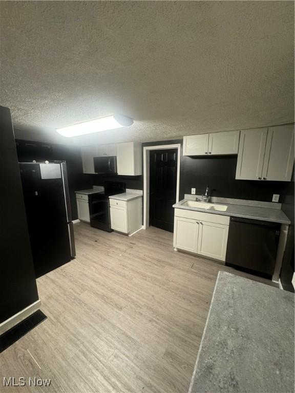 kitchen with a textured ceiling, white cabinetry, a sink, black appliances, and light wood-style flooring