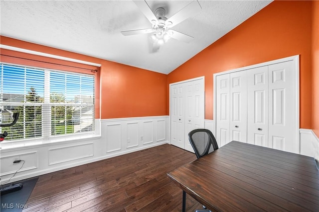 unfurnished office featuring ceiling fan, a textured ceiling, dark wood finished floors, a wainscoted wall, and vaulted ceiling