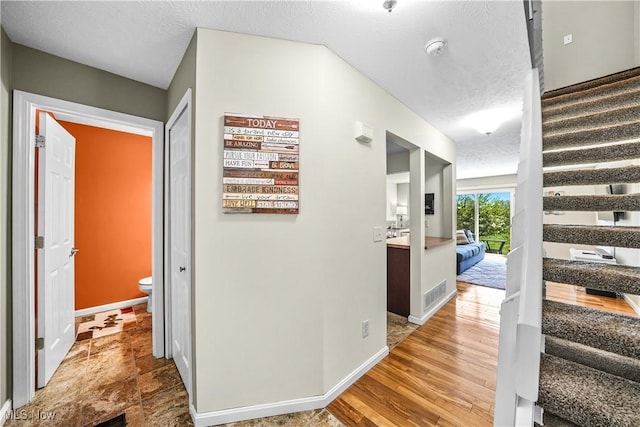hall featuring stairs, a textured ceiling, baseboards, and visible vents