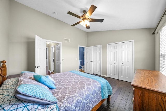 bedroom with visible vents, two closets, ceiling fan, dark wood finished floors, and vaulted ceiling