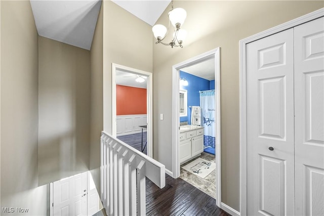corridor featuring an inviting chandelier, dark wood finished floors, and an upstairs landing