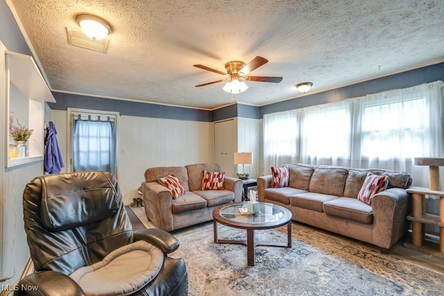 living area with ceiling fan, a textured ceiling, visible vents, wood finished floors, and ornamental molding
