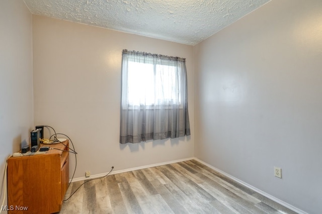 spare room featuring baseboards, a textured ceiling, and wood finished floors