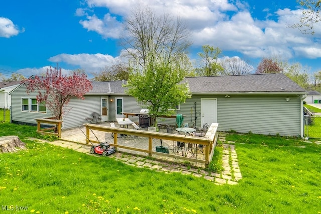 back of house with a lawn, a wooden deck, and roof with shingles