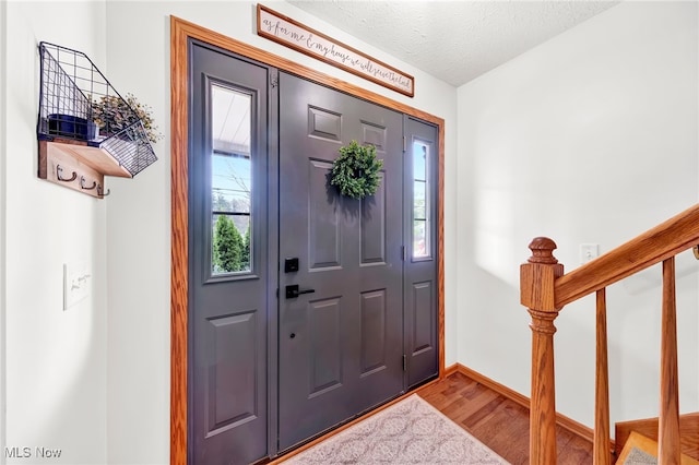 entrance foyer featuring baseboards, a textured ceiling, wood finished floors, and stairway