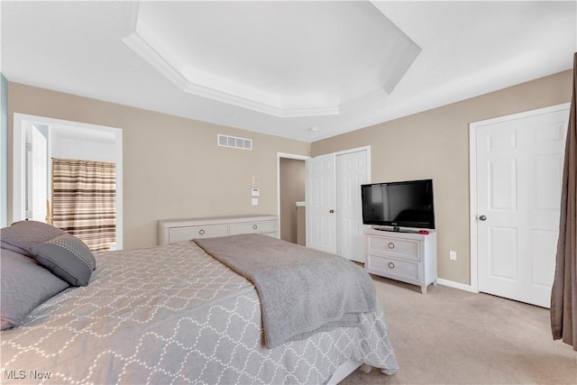 bedroom with baseboards, a tray ceiling, light colored carpet, and visible vents