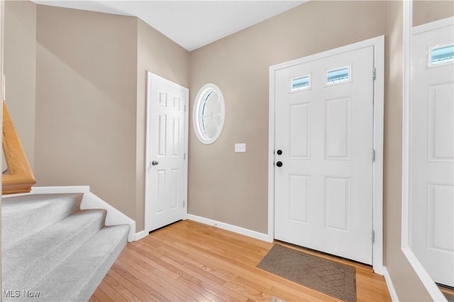 foyer featuring light wood-type flooring, baseboards, stairs, and a wealth of natural light